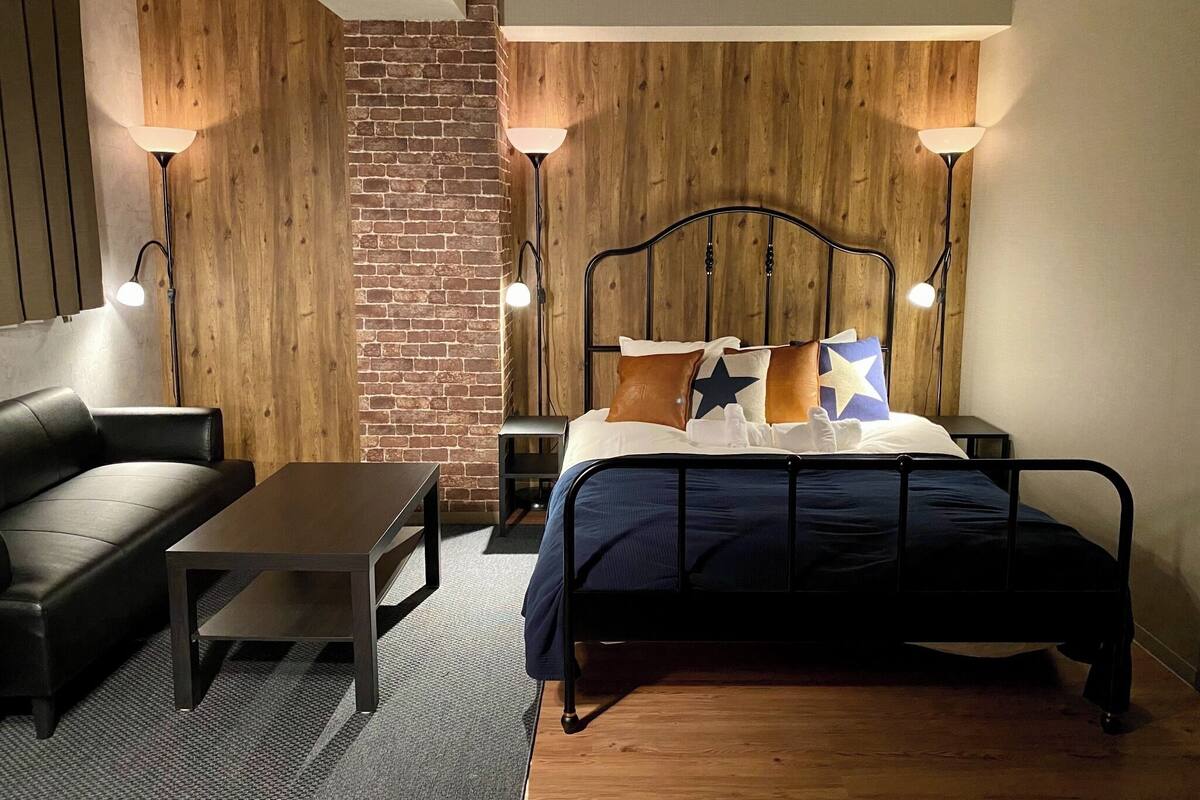 A bedroom with a bed, a nightstand, a lamp, a chair, and a small table.