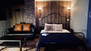 Un dormitorio con cama, mesita de noche, lámpara, sofá y pared de ladrillo.