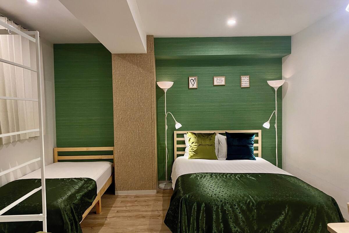 A room with two single beds, a wooden headboard, a green wall, and a white floor lamp.
