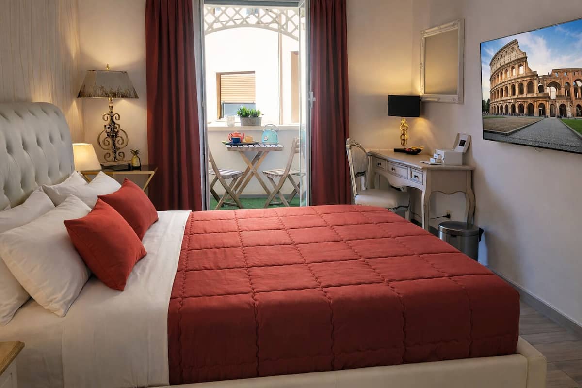 A hotel room with a bed, a desk, a chair, a TV, and a view of the Colosseum.