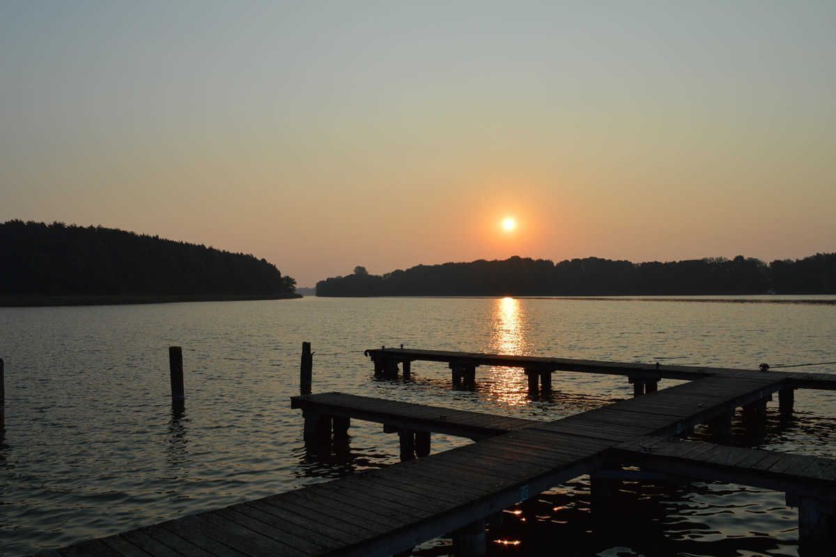 Ein Sonnenuntergang über einem ruhigen See mit hölzernen Stegen, die ins Wasser führen.