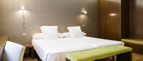 Una habitación de hotel moderna con una cama doble, mesitas de noche, un banco y un armario.
