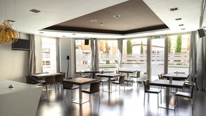 Un comedor moderno con mesas y sillas, ventanas amplias y un televisor de pantalla plana montado en la pared.