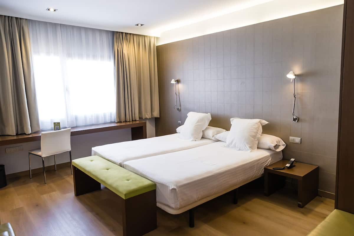 Une chambre d’hôtel avec un lit double, une banquette, un bureau et une chaise.