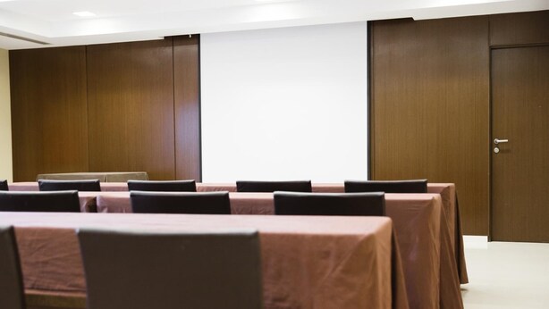Ein Konferenzraum mit langen Tischen und Stühlen, Holzvertäfelung an den Wänden und einer Tür.