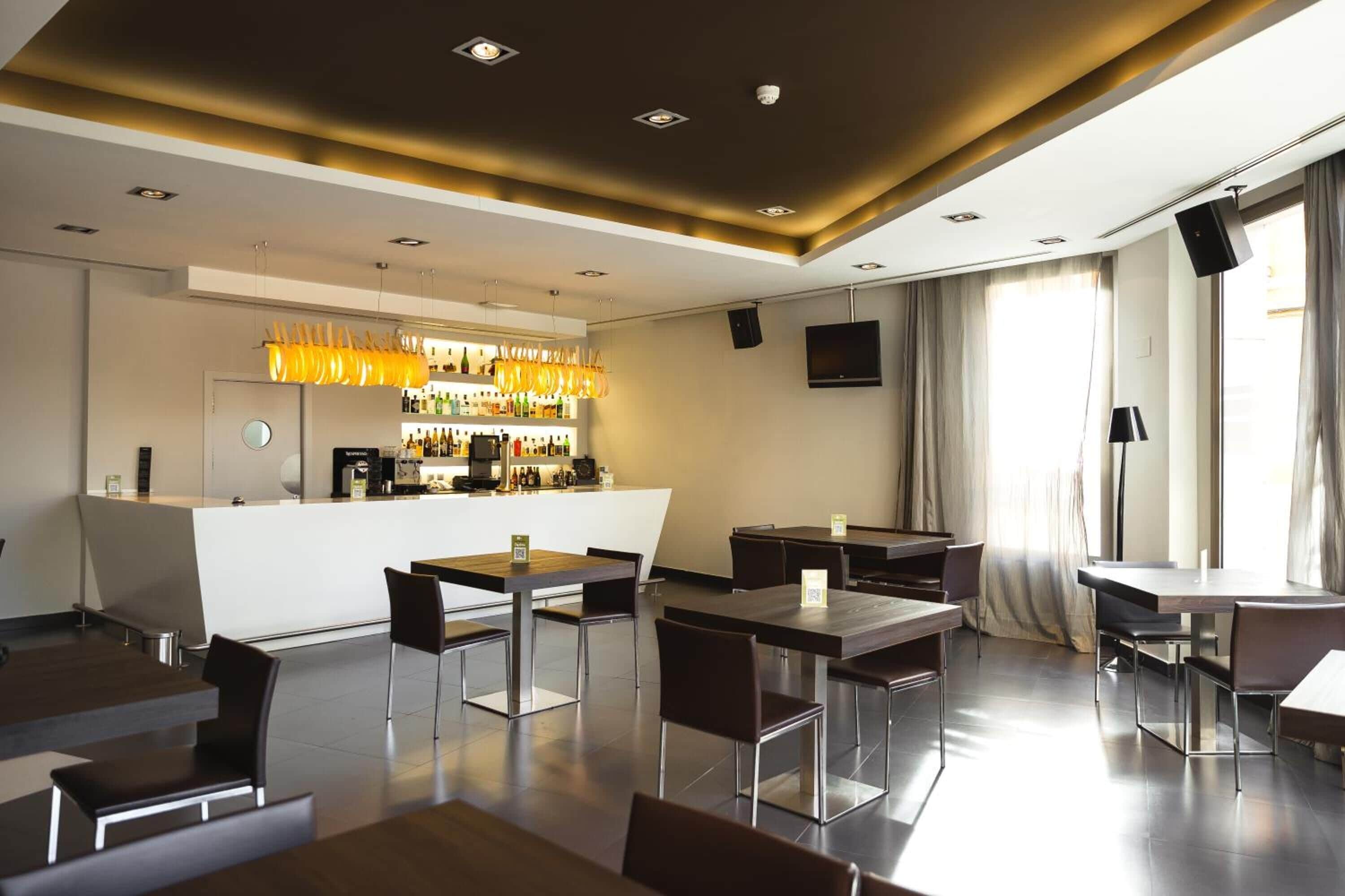 Un moderno vestíbulo de hotel con zona de bar, arreglos de asientos y un gran ventanal con cortinas.
