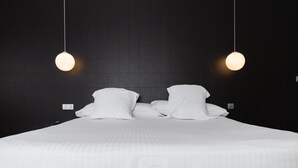 Una cama bien hecha con sábanas y almohadillas blancas, dos lámparas colgantes arriba y una pared oscura con un diseño de cuadrícula.