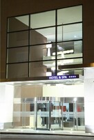 Entrada de um hotel com fachada de vidro, uma placa indicando que é um hotel e spa, e uma porta giratória.