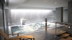 Ein moderner Wellnessbereich mit Whirlpool, Holzmöbeln und einer gefliesten Wand.