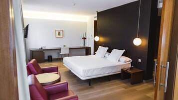 A modern hotel room with a bed, a desk, a chair, and a small table.