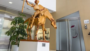 Un interior moderno con una gran escultura dorada de un jinete a caballo, una planta en maceta y la puerta de un ascensor de vidrio.
