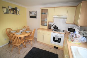A compact kitchen with a dining table, chairs, a stove, oven, and a microwave.