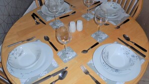 Mesa de madera redonda dispuesta para cuatro, con platos de estampado floral, cubiertos y cristalería.