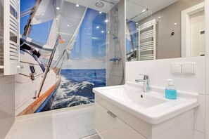 A modern bathroom with a large mirror, a white sink, and a shower area.