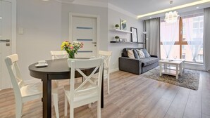 A modern living room with a dining area, featuring a round table, white chairs, a grey sofa, and a small white side table. - Flats For Rent - Aura Spa&Wellness (Gdansk)