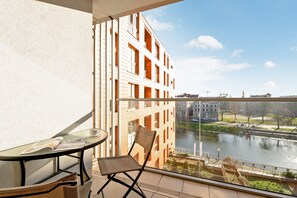 A balcony with a glass table and chair, overlooking a river and buildings.
