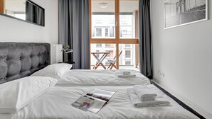 A modern hotel room with a large bed, a view of the city through large windows, and a framed picture on the wall. - Flats For Rent - Aura Spa&Wellness (Gdansk)