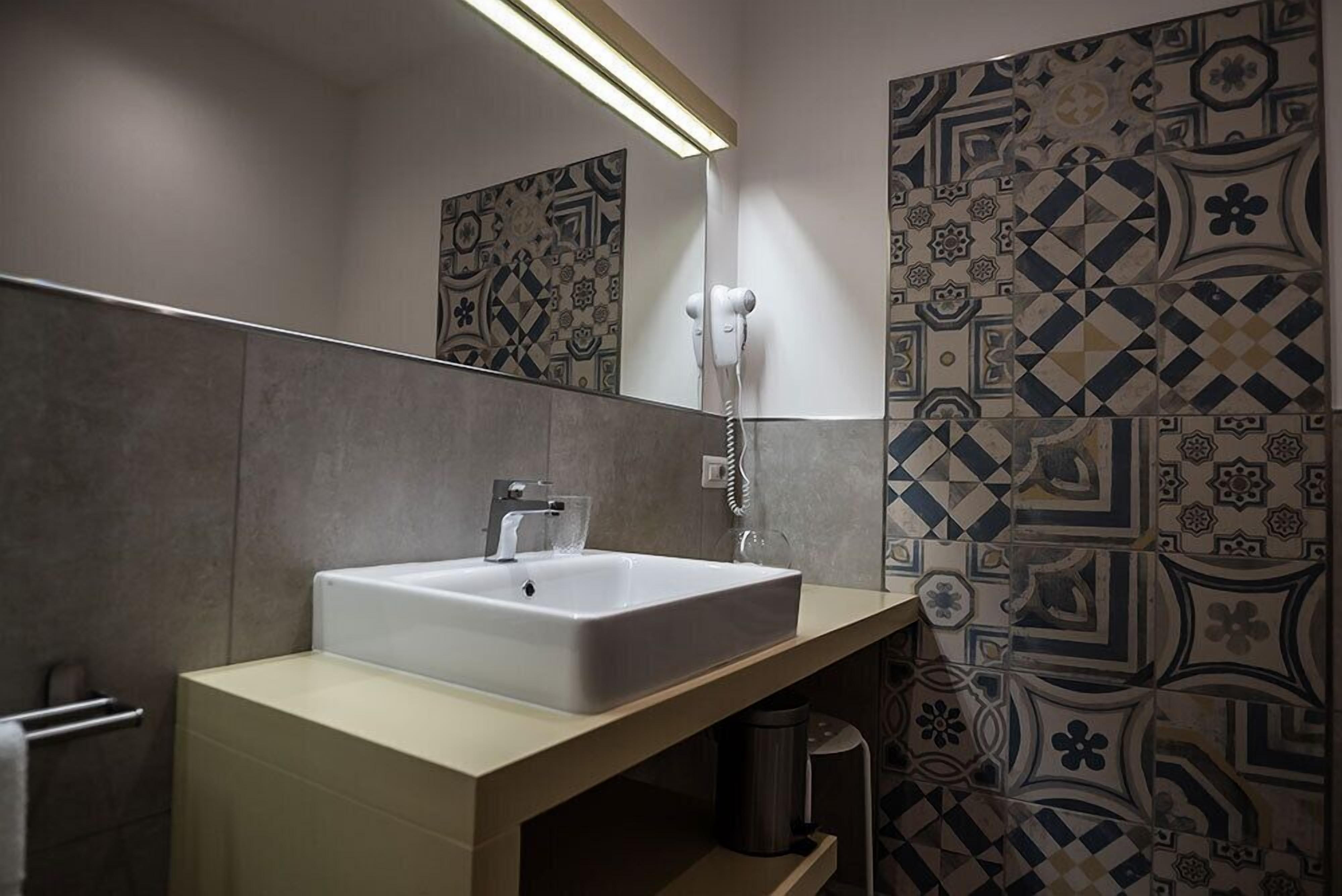 A bathroom with a white sink, a mirror, a telephone, and patterned tiles on the walls.