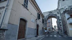 A street with a stone archway, buildings with signs, and a pedestrian crossing.