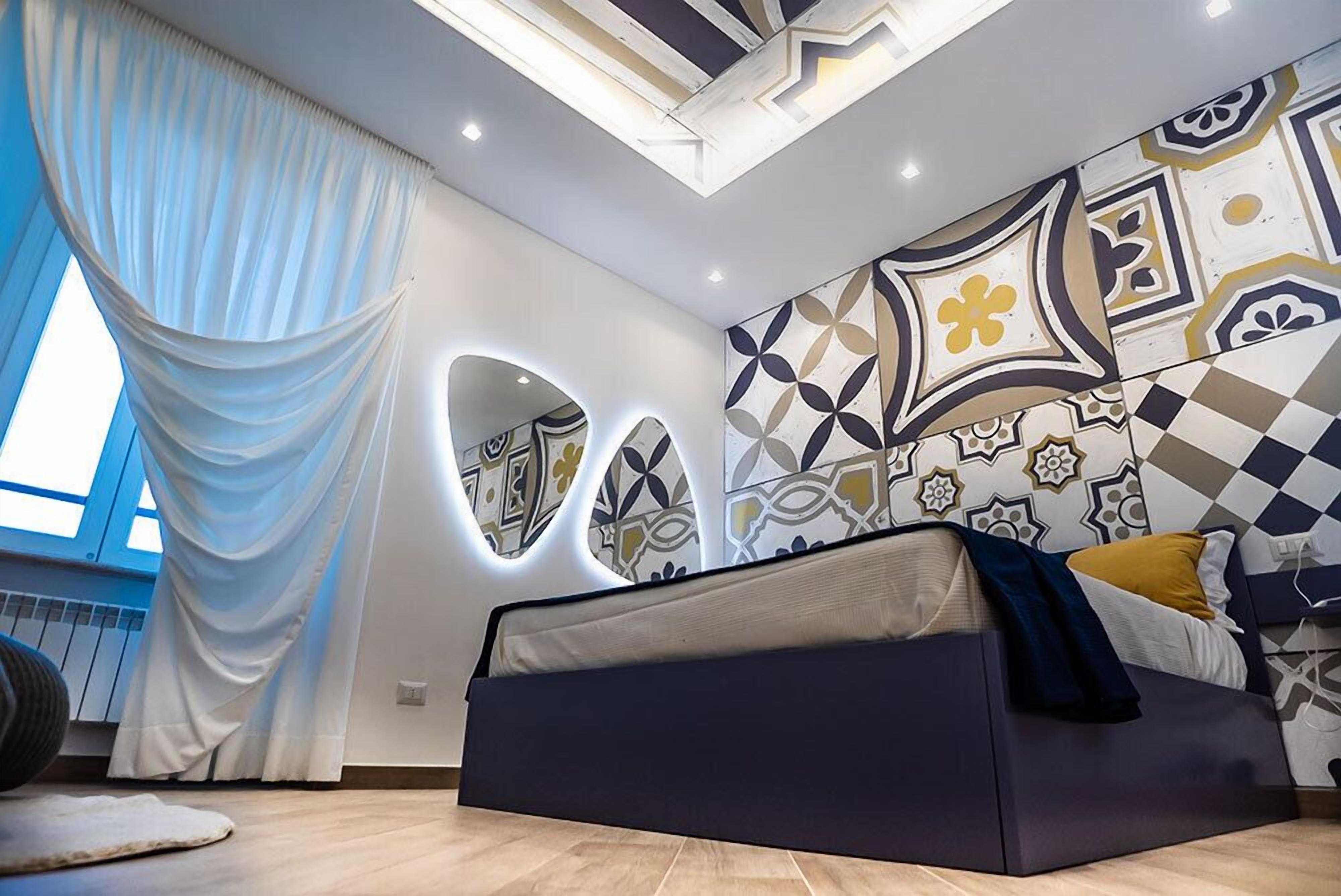 Ein modernes Schlafzimmer mit einem Bett, einem großen Fenster mit Vorhängen und einer Wand mit geometrischen Mustern.