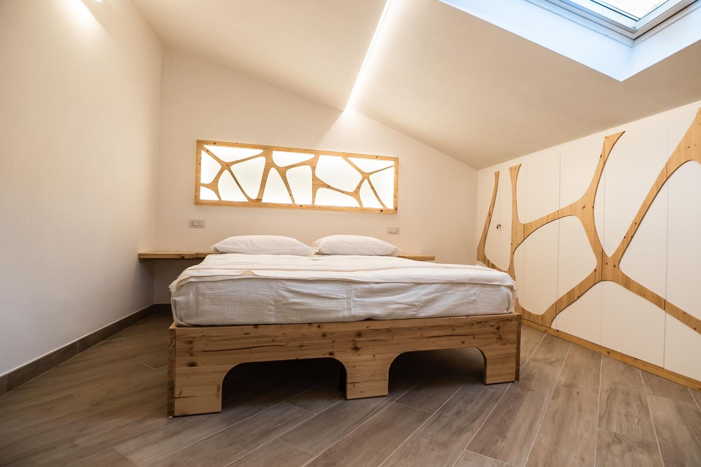 Un dormitorio moderno con estructura de cama de madera, tragaluz y diseño geométrico en la pared.
