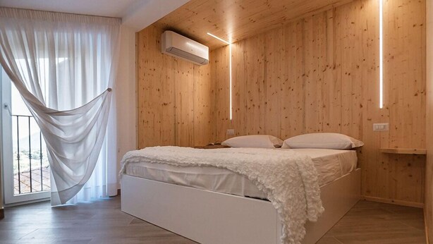 A bedroom with a wooden wall, a bed with white bedding, and a hanging white curtain.