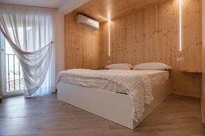 Un dormitorio con pared de madera, una cama con ropa de cama blanca y una cortina blanca colgada.