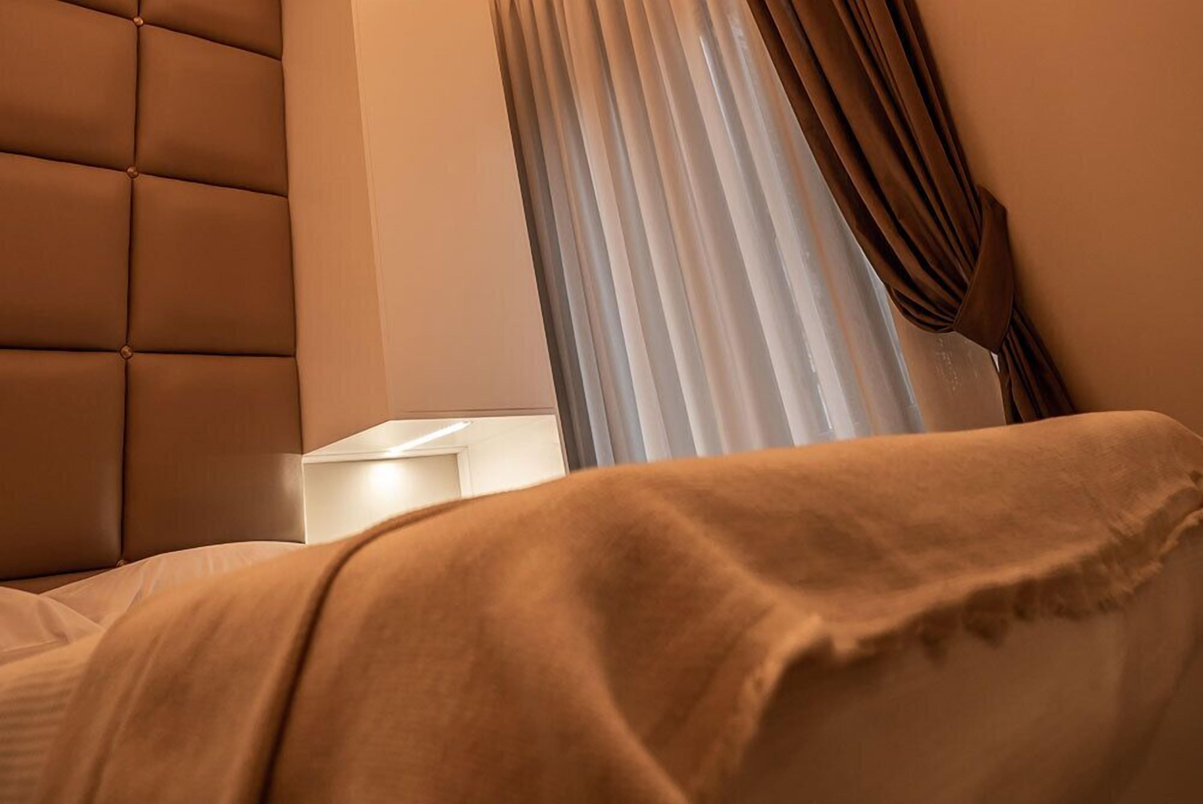 Quarto com cabeceira estofada, mesa de cabeceira e janela com cortinas.