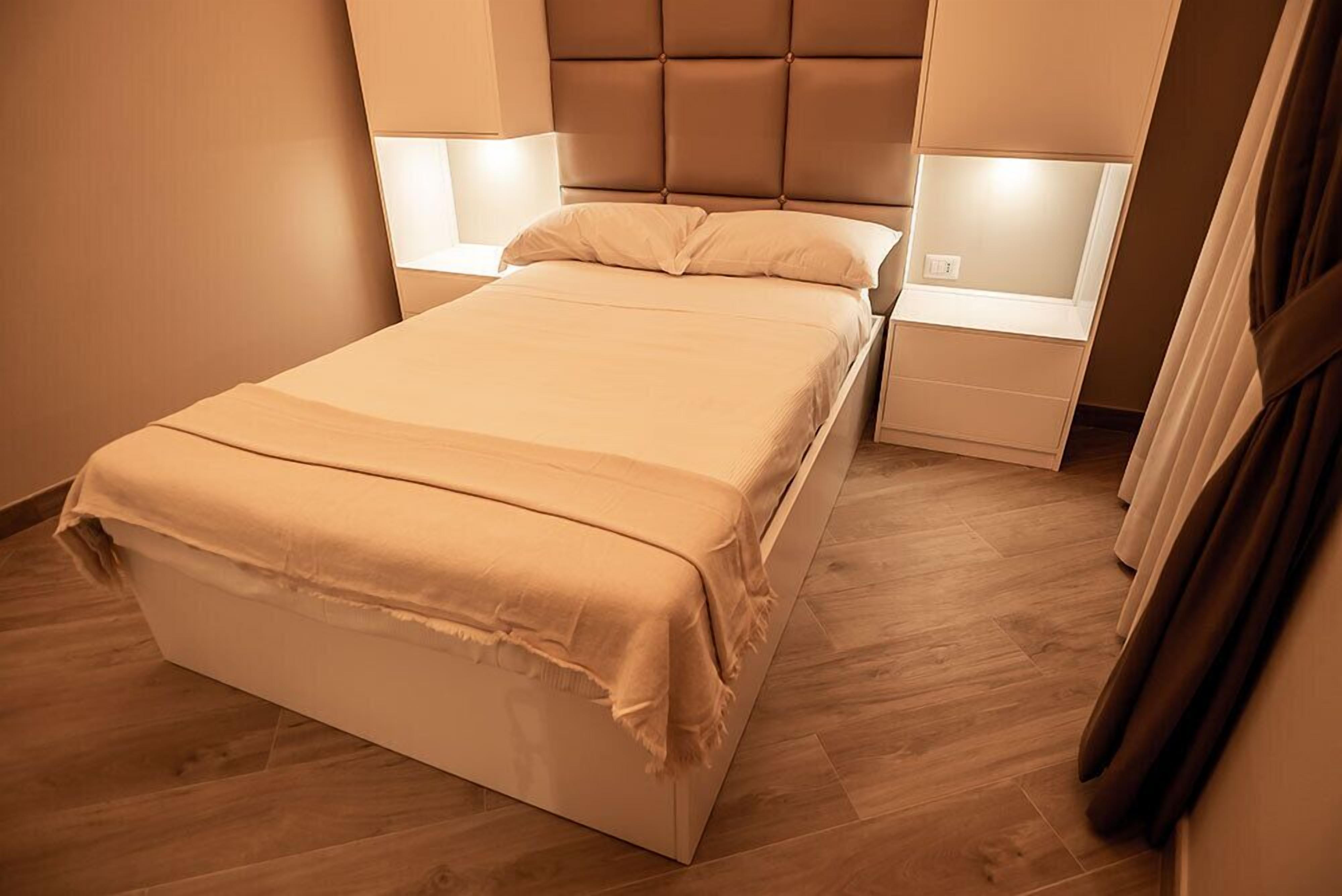 A neatly made bed with a headboard, two bedside tables with lamps, and a wooden floor.