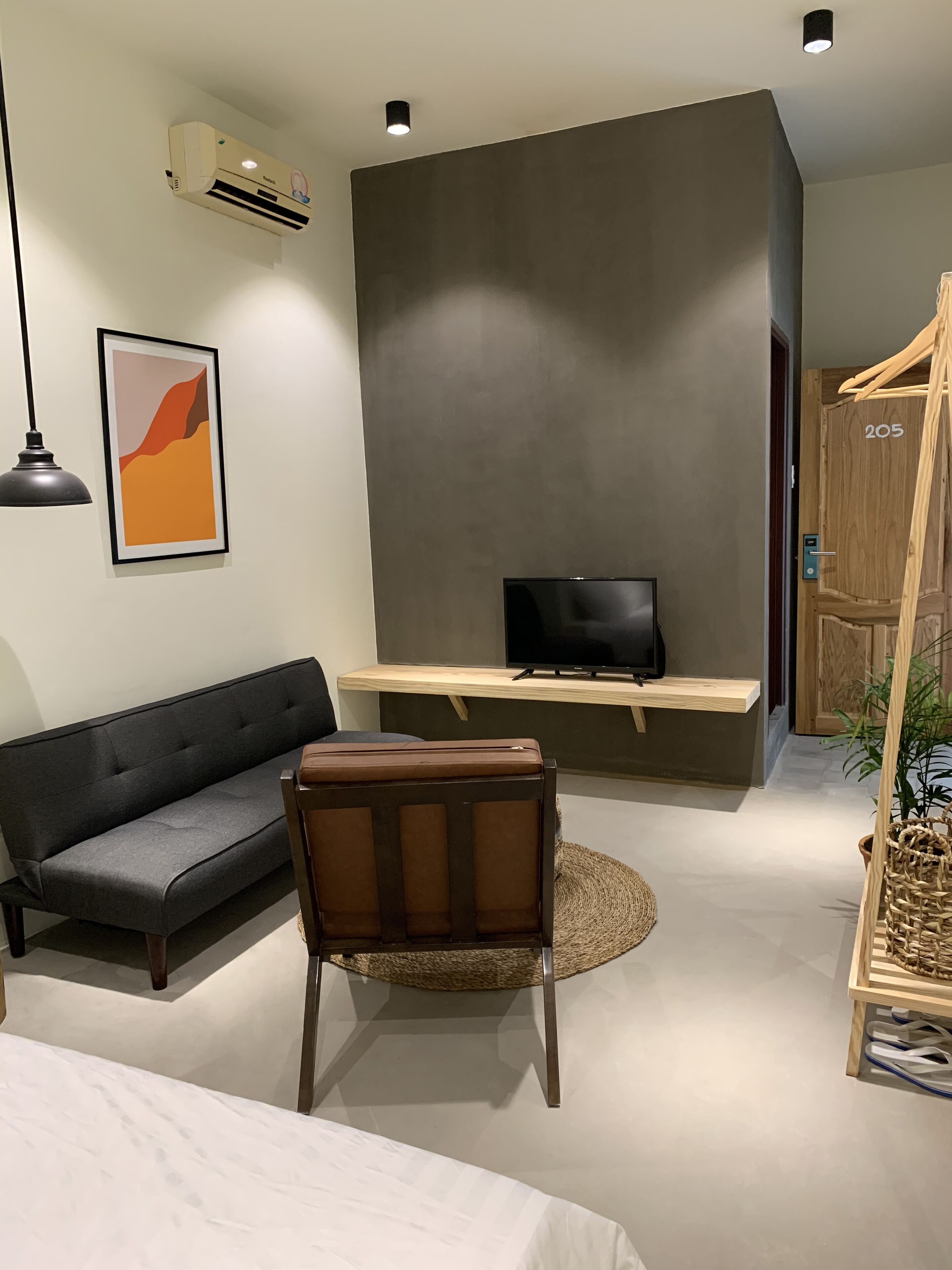 Ein modernes Zimmer mit einer Couch, einem Sessel, einem Fernseher auf einem Holzregal und einer hängenden Pflanze.
