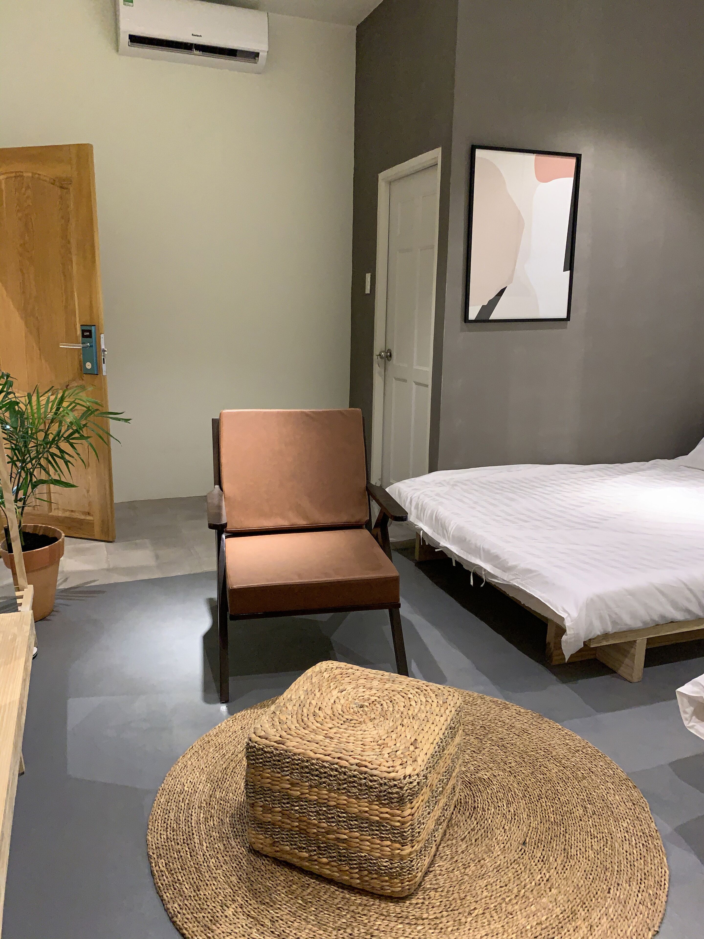 A bedroom with a bed, a chair, a woven basket, a potted plant, and a door.