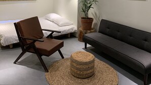 Une chambre moderne comprenant un lit, un canapé, une chaise, une plante en pot, une lampe suspendue et un climatiseur.