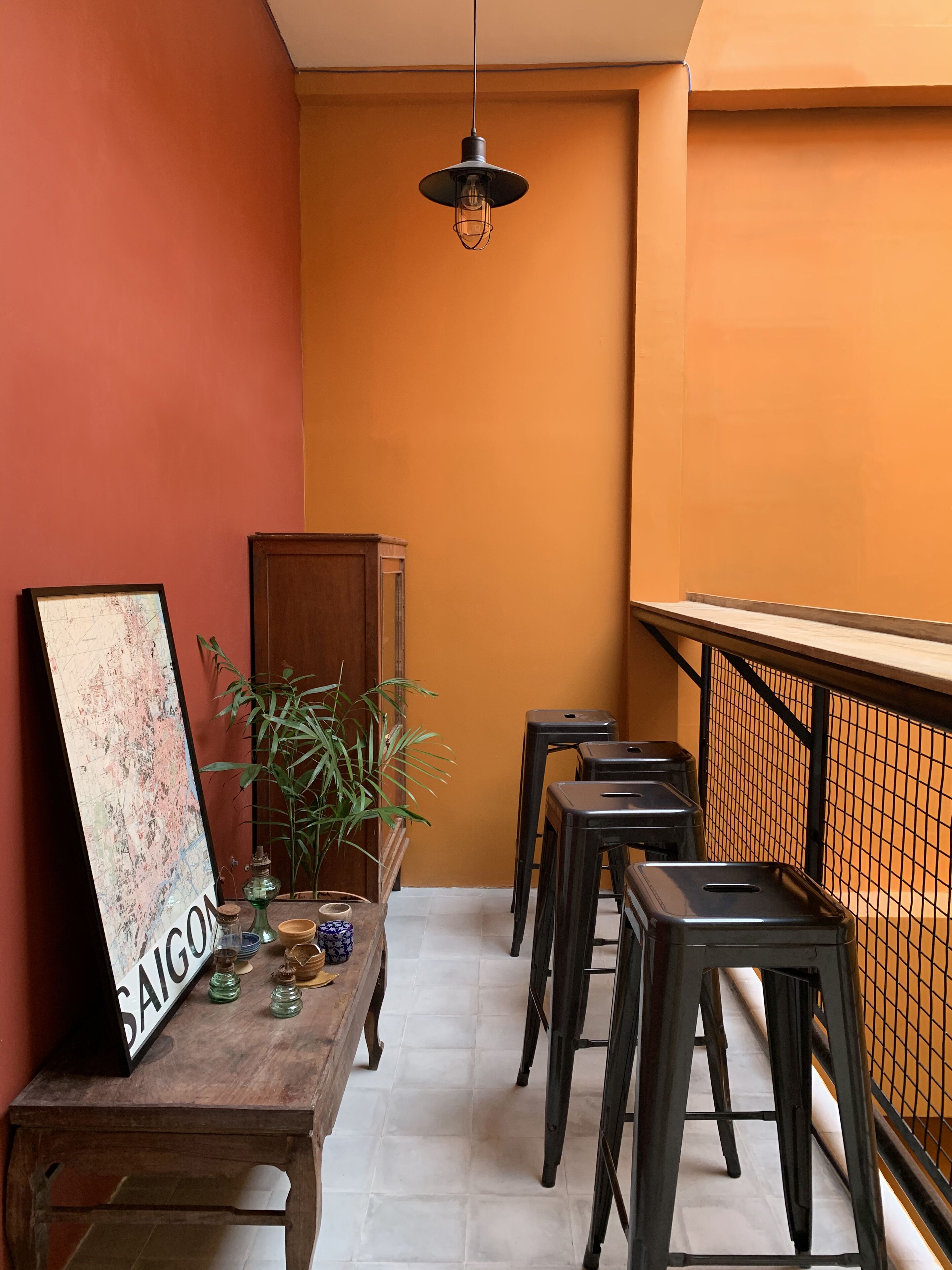 Una habitación pequeña y acogedora con una mesa de madera, un mapa y una planta en maceta. Hay tres taburetes negros y una lámpara colgante.