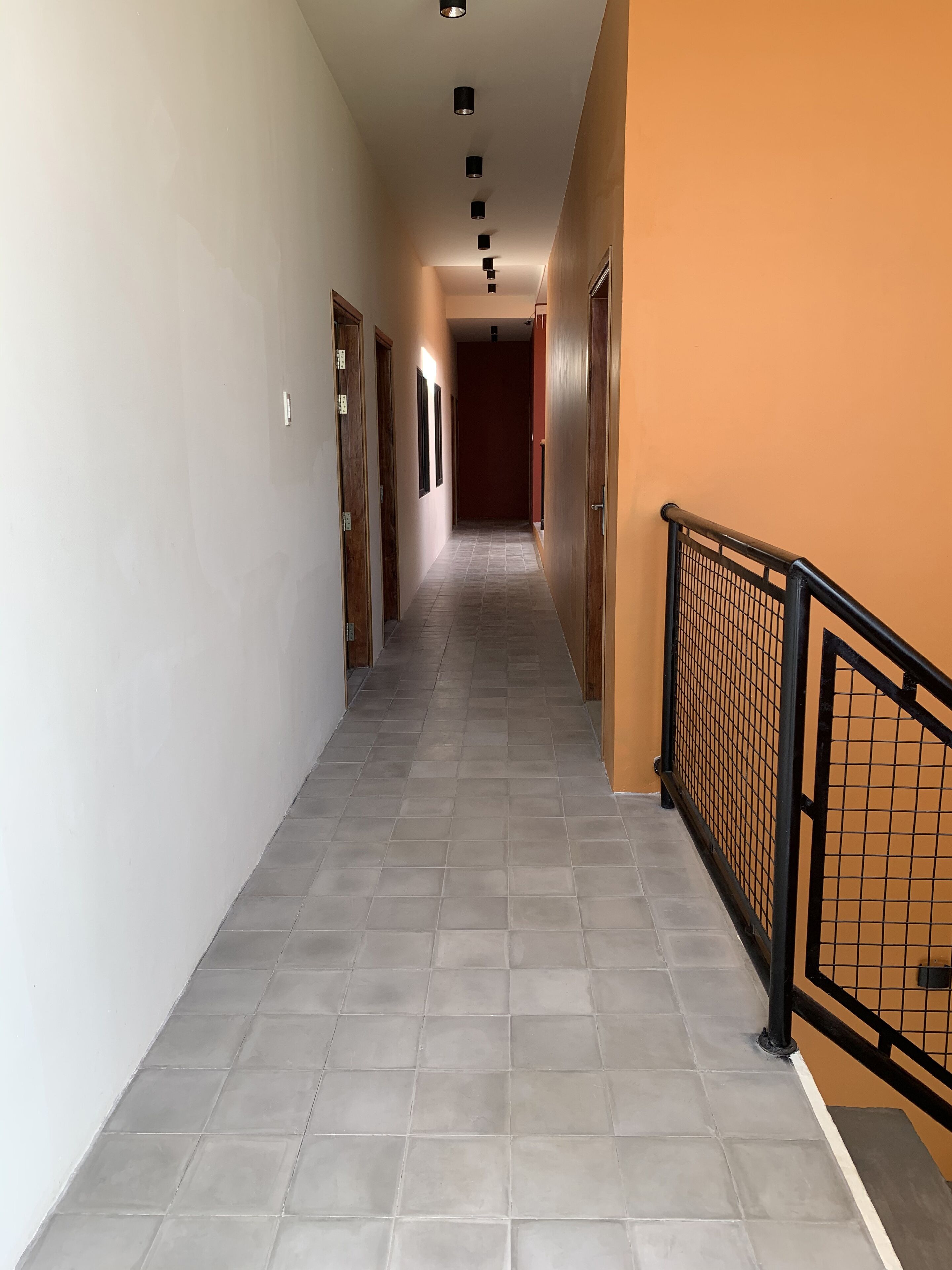 A hallway with tiled flooring, wooden doors, and a black metal railing.