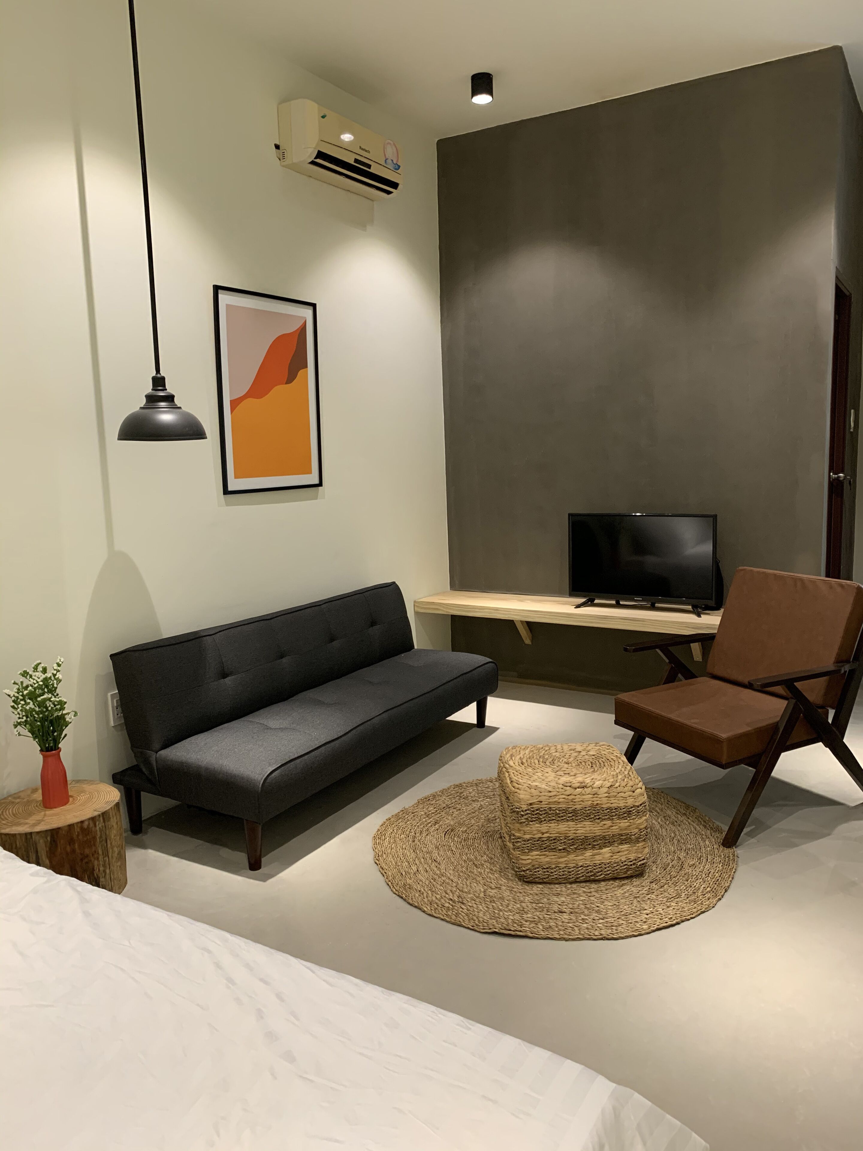 A modern bedroom with a sofa, a chair, a TV, and a round woven rug.
