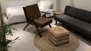 Une chambre à coucher moderne et minimaliste, comprenant un lit, un canapé, une chaise et un pouf rond en fibres tressées.