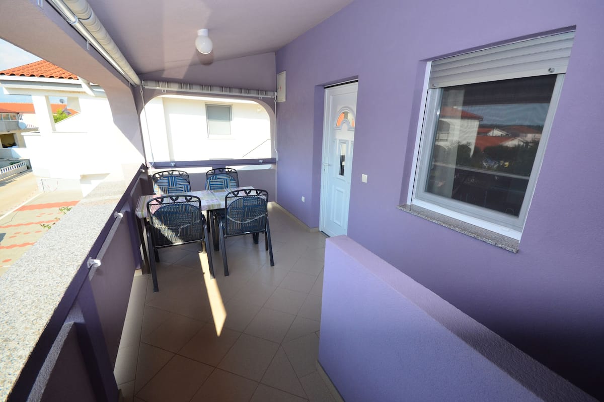 A balcony with a table and chairs, a window, and a door.