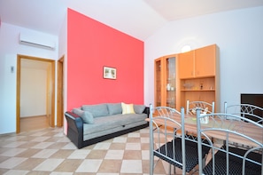 A living room with a sofa, a dining table with chairs, a red accent wall, and a wooden cabinet. - Apartments Brandis (Vir)