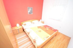 A bedroom with a bed, a nightstand, a lamp, a picture on the wall, and a striped rug. - Apartments Brandis (Vir)