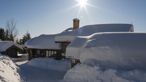 Un chalet enneigé, doté d’une cheminée, d’une façade en bois et surplombant un ciel dégagé.