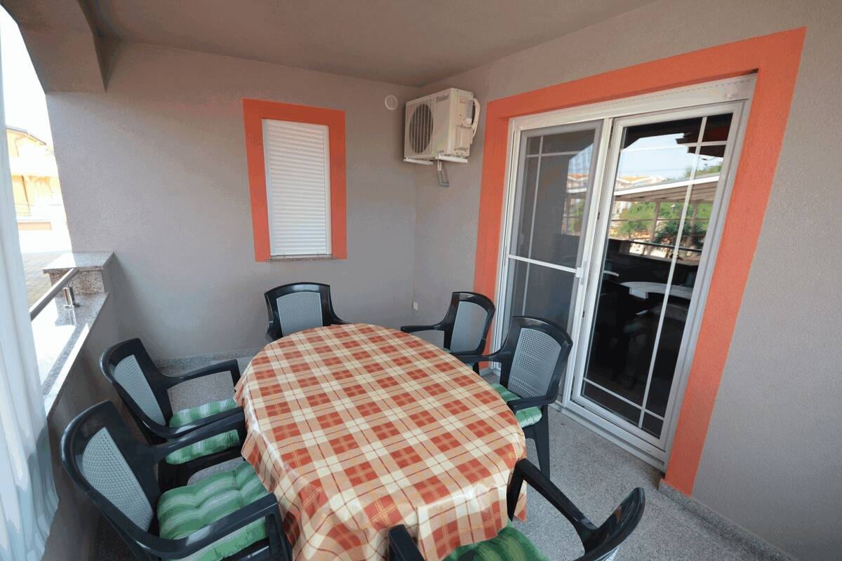 A balcony with a table and chairs, an air conditioning unit, a window with blinds, and a sliding glass door.