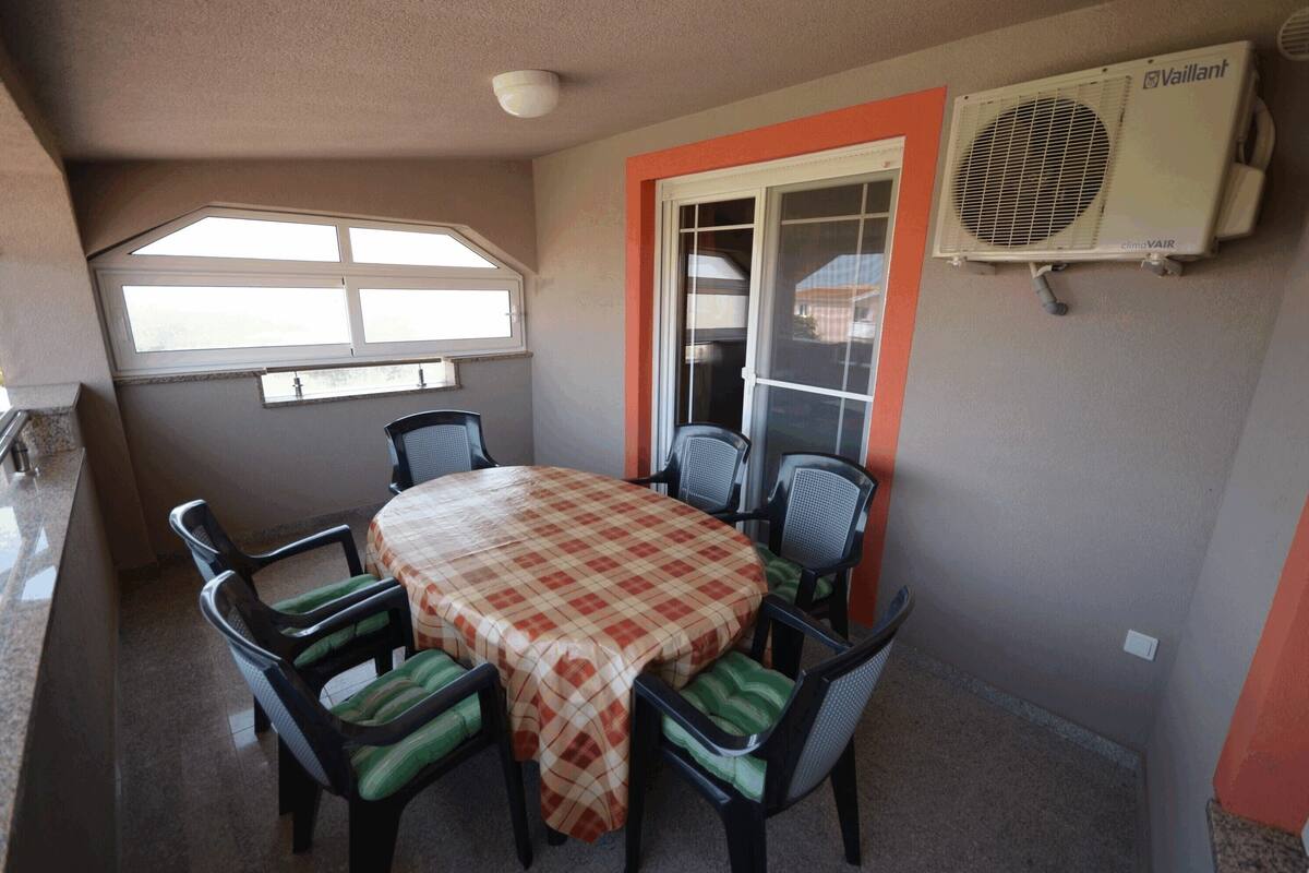 A dining area with a table covered by a checkered tablecloth, surrounded by chairs with green cushions.