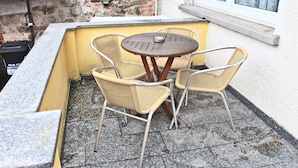 A small outdoor seating area with a round table and four wicker chairs, a brick wall, and a window with curtains. - Pixie Home (Hanau)