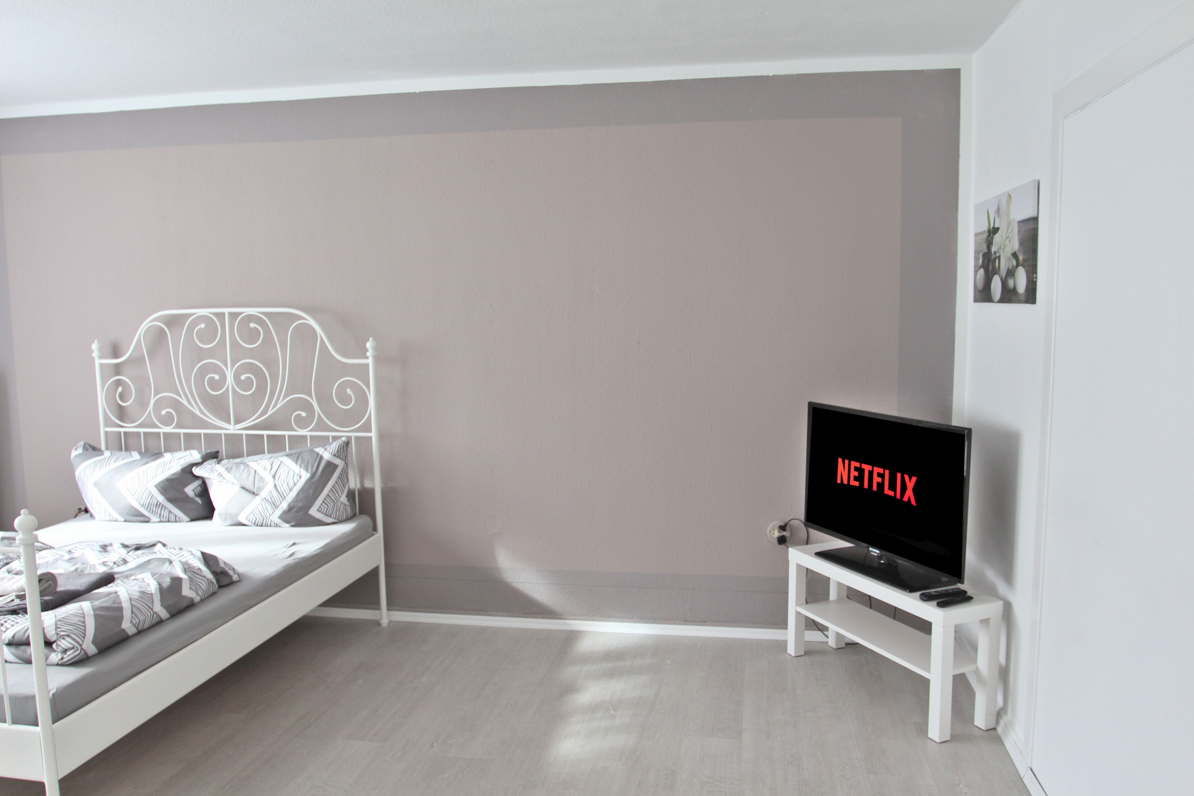 Ein Schlafzimmer mit einem Bett, einem Fernseher auf einem Schrank und einem an der Wand hängenden Bild.