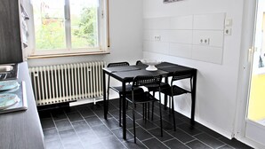 A kitchen with a dining table, chairs, a radiator, a window, and a clock on the wall. - Pixie Home (Hanau)