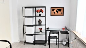 A modern office space with a black metal desk, a white chair, a black metal shelving unit with white storage boxes, a world map artwork, and a radiator. - Pixie Home (Hanau)