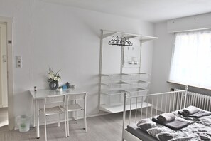 Een kamer met een bed, een bureau met stoelen, een kledingrek en een radiator.