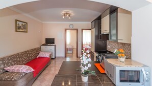 Una sala de estar moderna con un sofá, una manta roja, una mesa de centro, un televisor y una zona de cocina con un microondas y un tostador.