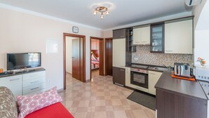 Un espacio habitable compacto con kitchenette, televisor y cama con almohada de diseño rojo y blanco.