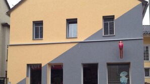 A two-story building with a yellow and grey facade, multiple windows, and a red fire hydrant on the ground floor. - Mixie Home (Hanau)